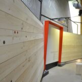 Ein Blick durch den Bauzaun - Fotoausstellung Ein Haus wie damals. Bauen mit Holz, Lehm und Reet seit 5.000 Jahren im archeoParc Schnalstal <br />Fotografie del cantiere di una capanna preistorica di Gianni Bodini nascoste nella parete della mostra La casa di Ötzi. La ricostruzione di una capanna preistorica presso larcheoParc della val Senales<br /> Photography exhibition on a Cupper Age house reconstruction and its building materials still used in creating modern environmentally sustainable buildings at archeoParc Val Senales<br /><br />July-November 2016