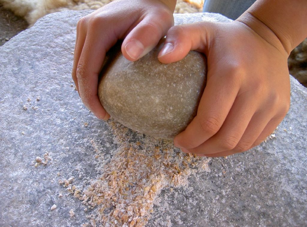 Mehl mahlen auf der Steinmühle im Freilichtbereich des archeoParc SchnalstalMacinare il grano con la macina di pietra nellarea allaperto dell'archeoParcGrinding flour on the Copper Age stone mill at the open-air area of archeoParc