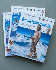 Cover des Buches „Die Gletschermumie. Mit Ötzi auf Entdeckungsreise durch die Kupferzeit“ von Gudrun Sulzenbacher und Angelika FleckingerCopertina del libro „La mummia dei ghiacci. Con Ötzi alla scoperta dell' età del Rame“ di Gudrun Sulzenbacher e Angelika FleckingerCover of the book „The Glacier Mummy. Discovering the Copper Age with the Iceman” from Gudrun Sulzenbacher and Angelika Fleckinger